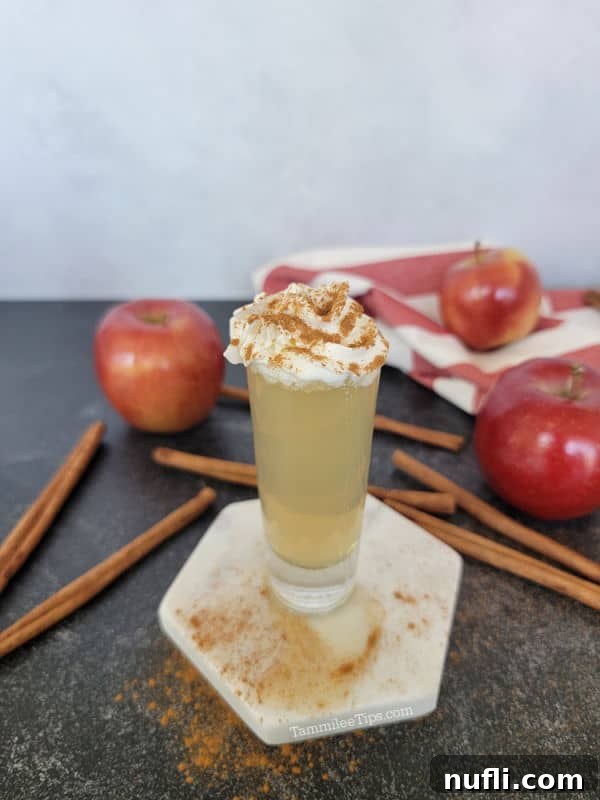 Apple Pie In A Shot Glass 7 Apple pie shot with whipped cream and cinnamon next to cinnamon sticks and red apples