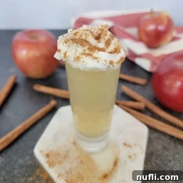 Apple Pie In A Shot Glass 8 Apple pie shot garnished with whipped cream and cinnamon next to cinnamon sticks and red apples