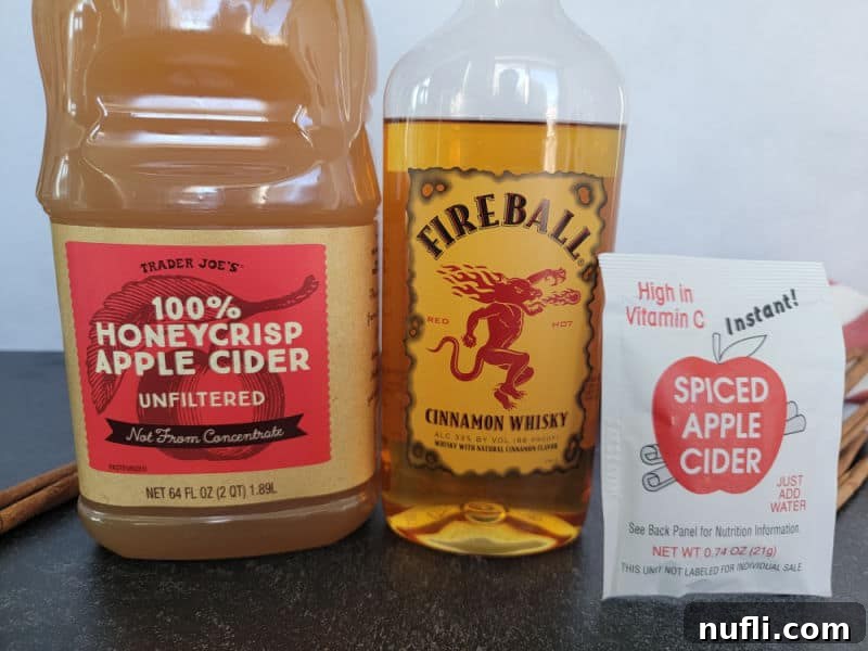 Ultimate Fireball Apple Cider 3 Trader joe's apple cider container, Fireball cinnamon whisky bottle, and spiced apple cider mix on a counter with cinnamon sticks.