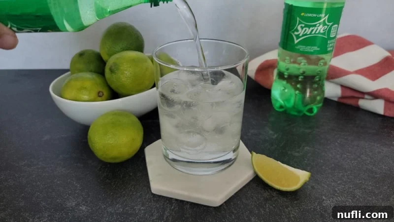 Sprite pouring into a cocktail glass next to a bowl of limes