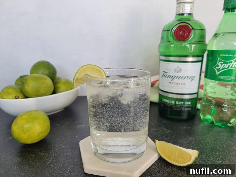 Gin and Sprite garnished with a lime next to a bottle of gin, sprite, and a bowl of limes