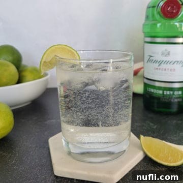 Gin and Sprite cocktail garnished with a lime slice next to a bowl of limes