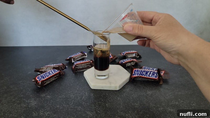 Baileys Irish Cream pouring over a bar spoon to create the top layer in a Snickers shot, highlighting the careful layering technique.