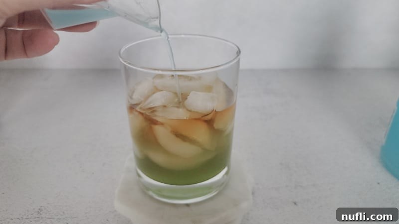 Gamma Ray Gulp 5 Blue hpnotiq pouring over Hennessey in a cocktail glass