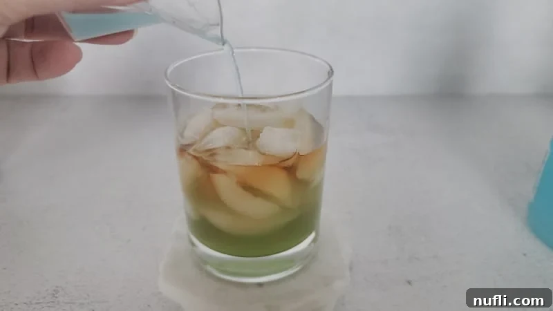 Emerald Fury Fuel 5 Blue hpnotiq pouring over Hennessey in a cocktail glass