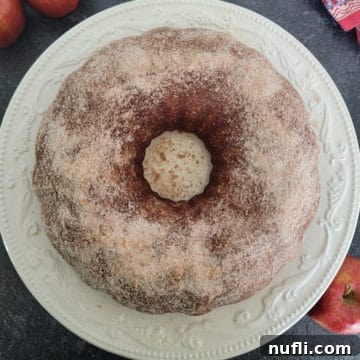 Apple Cider Donut Cake on a white plate with apples next to it