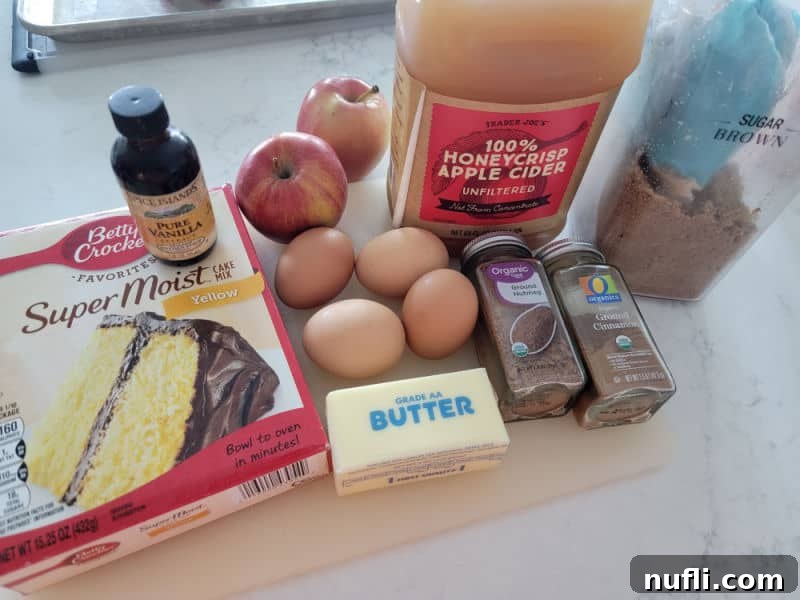 A collection of ingredients for Apple Cider Donut Cake, including yellow cake mix, vanilla extract, eggs, fresh apples, apple cider, brown sugar, butter, nutmeg, and cinnamon, neatly arranged on a rustic cutting board.