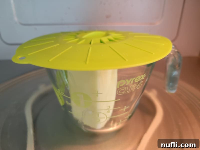 A microwave-safe measuring cup with melted butter, partially covered by a splatter lid, demonstrating a useful kitchen tool.