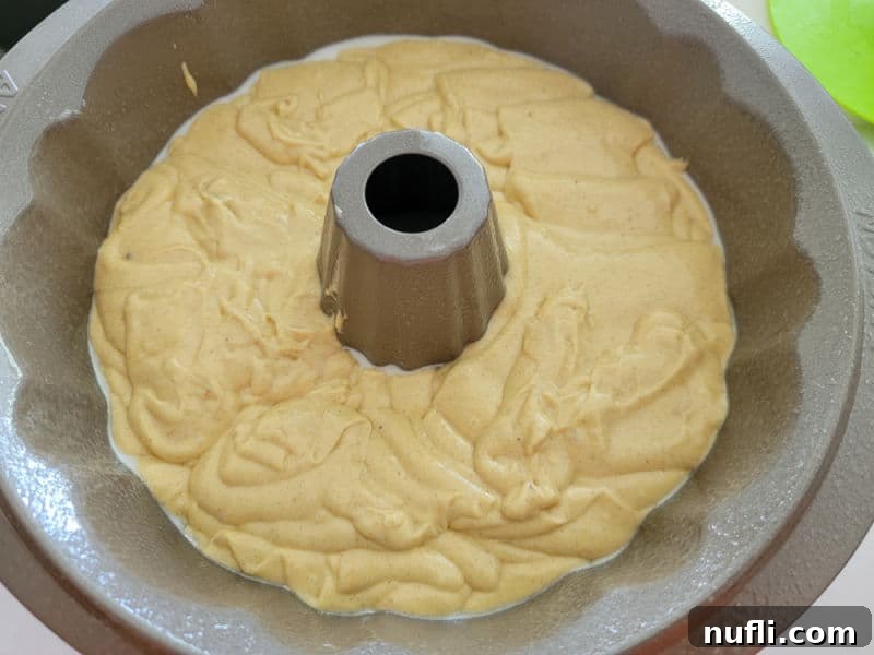 The smooth apple cider donut cake batter poured into a meticulously greased and floured Bundt cake pan, ready for baking to create its elegant shape.