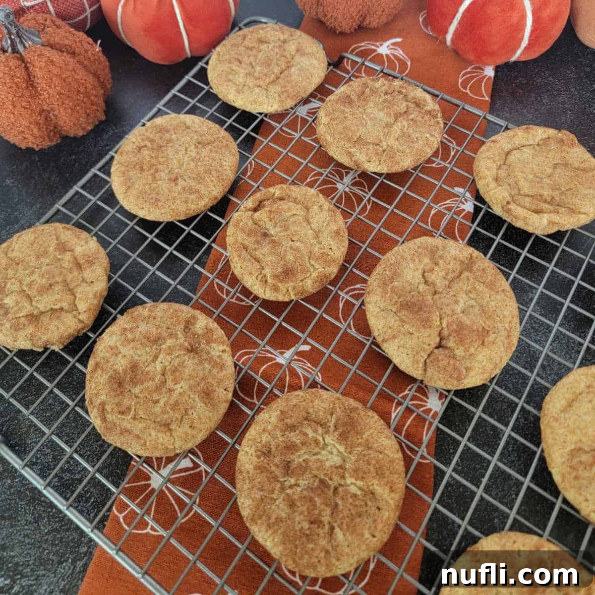 Pumpkin Snickerdoodles on a wire rack over a pumpkin napkin with cloth napkins in the background