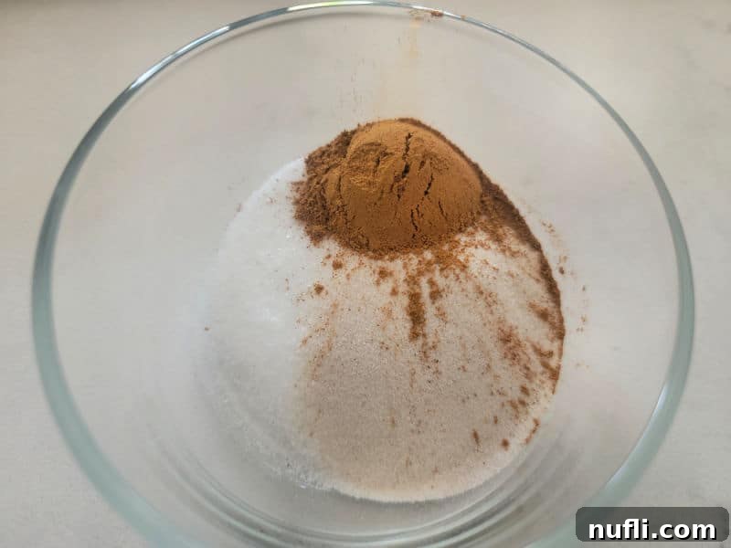 A small glass bowl containing a mix of cinnamon and granulated sugar, ready for coating the apple cider cookie dough.