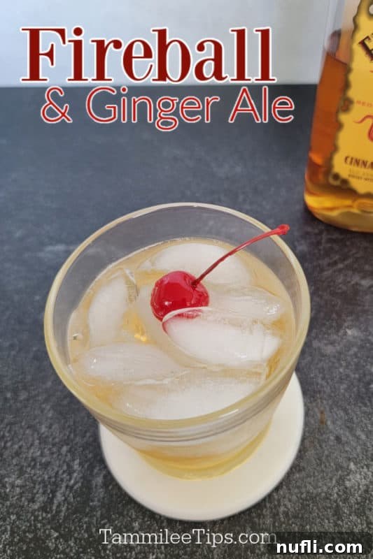 Cinnamon Ginger Sparkler 2 Fireball & Ginger Ale cocktail garnished with a cherry, with a partial Fireball whiskey bottle in the background