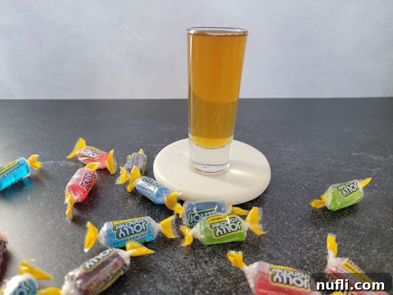 Jolly rancher shot on a white coaster surrounded by jolly rancher candy