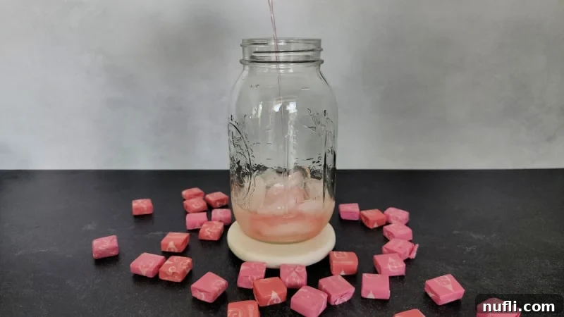 Pink Starburst Shots and Cocktails 4 Sour watermelon pouring into a mason jar surrounded by pink starburst candies