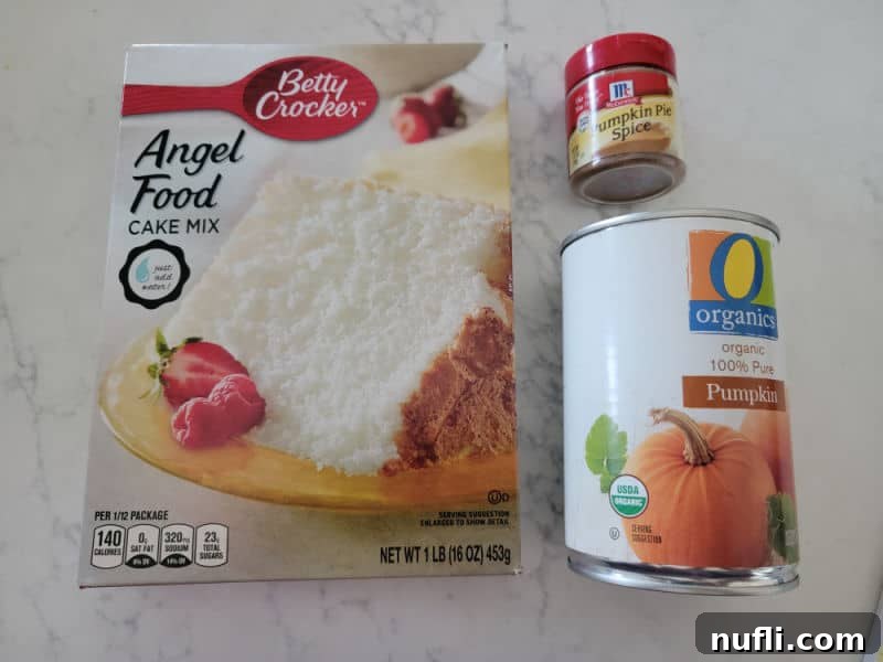 Key ingredients for pumpkin angel food cake: a box of angel food cake mix, a jar of aromatic pumpkin pie spice, and a can of smooth pumpkin puree, neatly arranged to inspire easy baking.