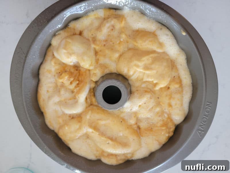 The rich, orange pumpkin angel food cake batter smoothly poured into a fluted Bundt cake pan, ready for baking and promising a beautiful dessert.