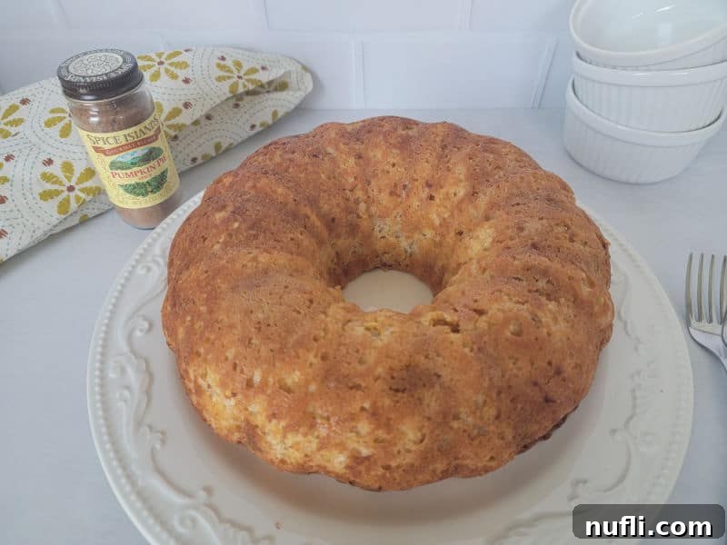 A beautifully baked pumpkin angel food cake presented on a pristine white cake stand, with a jar of pumpkin pie spice and a stack of bowls in the background, ready for serving a delightful fall treat.