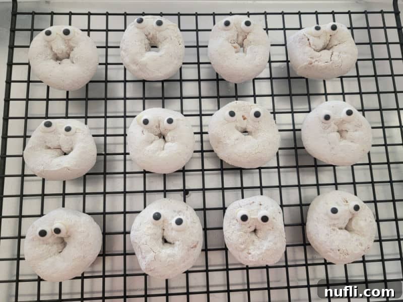 Powdered sugar donuts with candy eyes on a metal drying rack