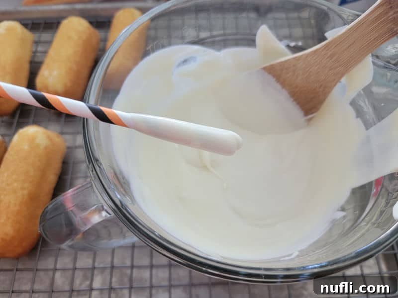 Straw dipping into a glass batter bowl filled with vanilla candy coating, preparing for Mummy Twinkies