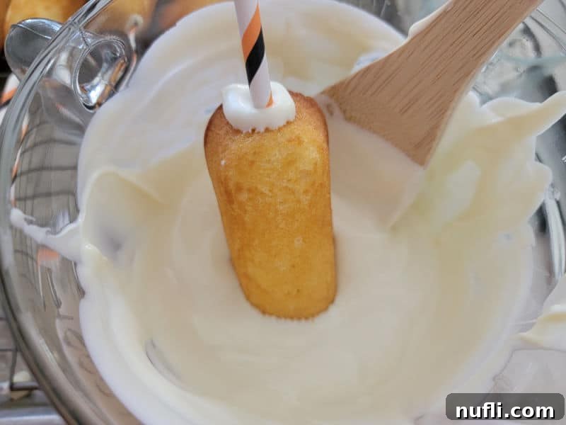 Twinkies dipping into melted vanilla bark, the crucial step for their mummy transformation