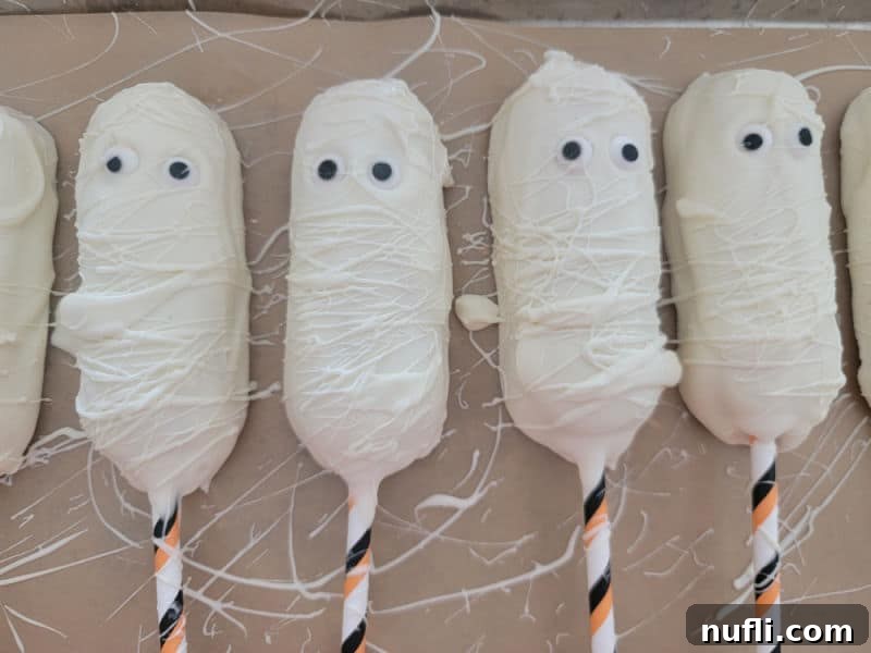 Mummy Twinkies lined up on parchment paper, waiting for their final touches