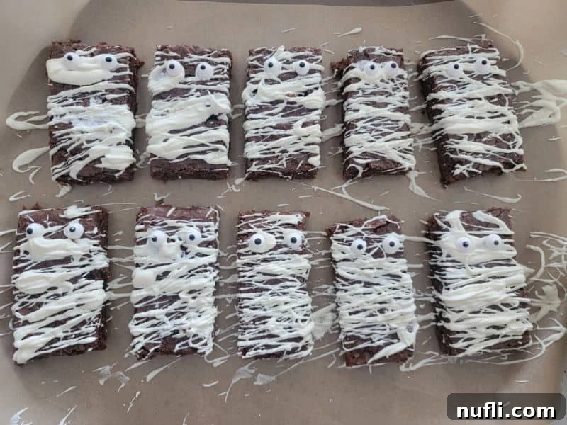 Mummy Brownies mid-decoration on parchment paper, with white chocolate bandages