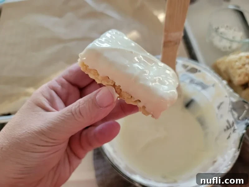 Monster Mummy Krispie Treats 4 Hand holding a rice krispie treat that has been dipped in white chocolate above a bowl, illustrating the dipping process.