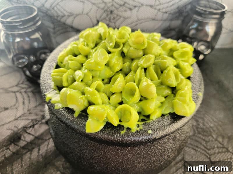 Green pasta shells and cheese in a black cauldron with skeleton glasses