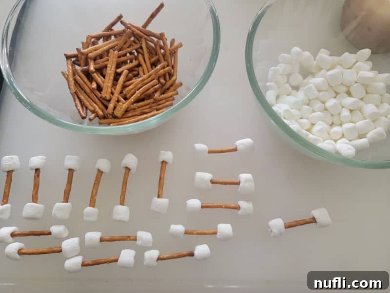 Pretzel sticks and mini marshmallows in bowls next to completed pretzel bones, ready for assembly