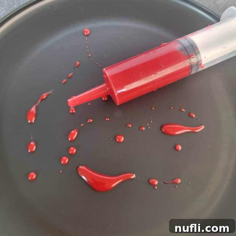 Realistic Edible Blood 2 Edible Blood in a plastic syringe on a black plate with edible blood splatters