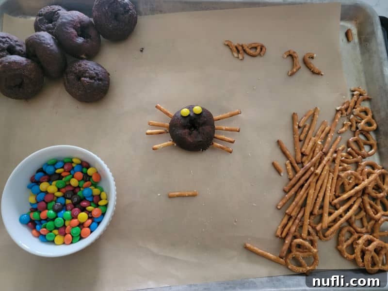 Close-up of a spider doughnut being assembled with pretzel pieces for legs and mini M&Ms for eyes