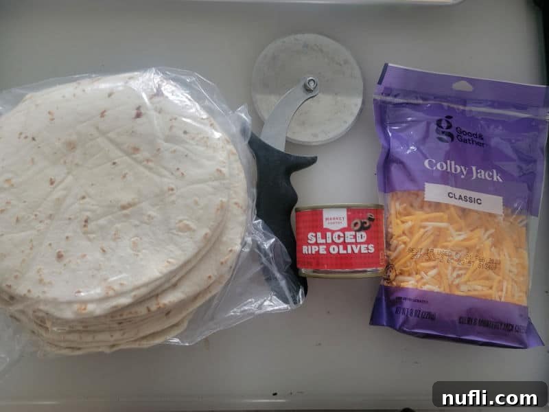 Tortillas, pizza cutter, sliced black olives and colby jack shredded cheese on a cutting board