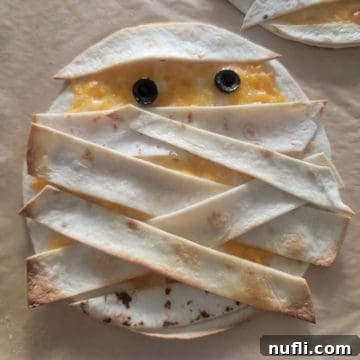 Mummy Quesadilla with black olive eyes on parchment paper