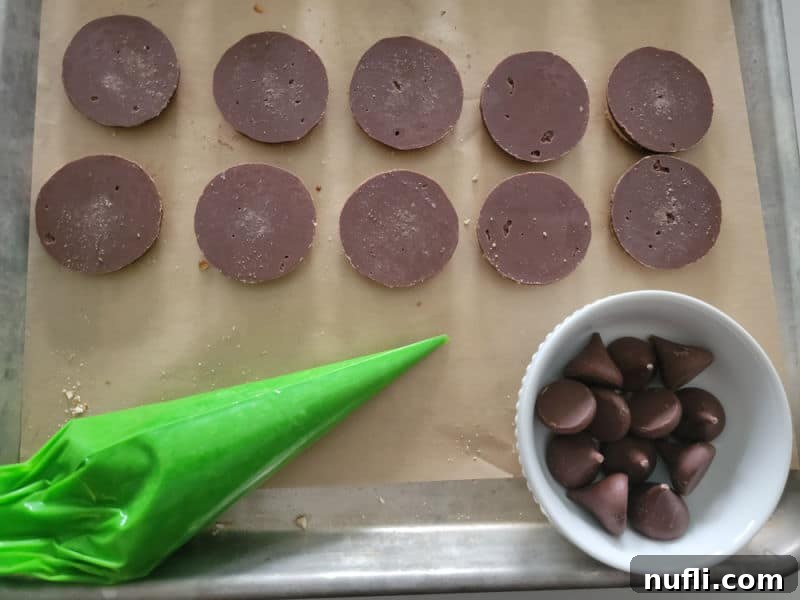 Shortbread cookies on parchment paper with green icing and Hershey Kisses ready to be assembled into witch hats
