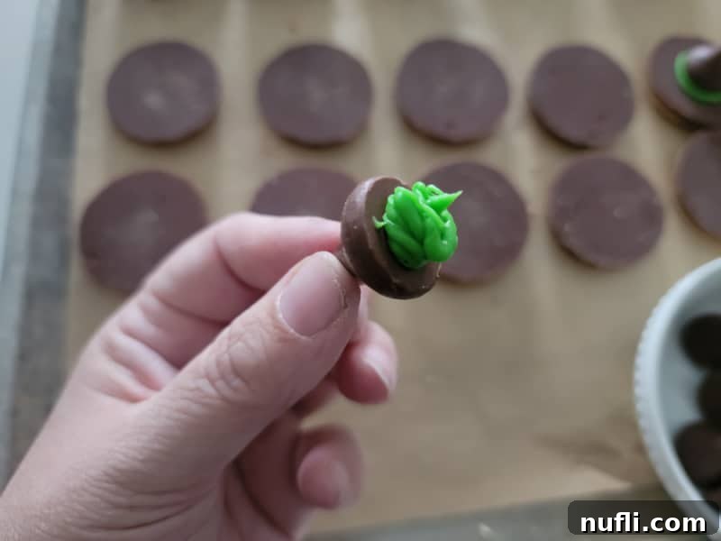 Green icing being spread on the bottom of a Hershey's Kiss for witch hat cookies assembly