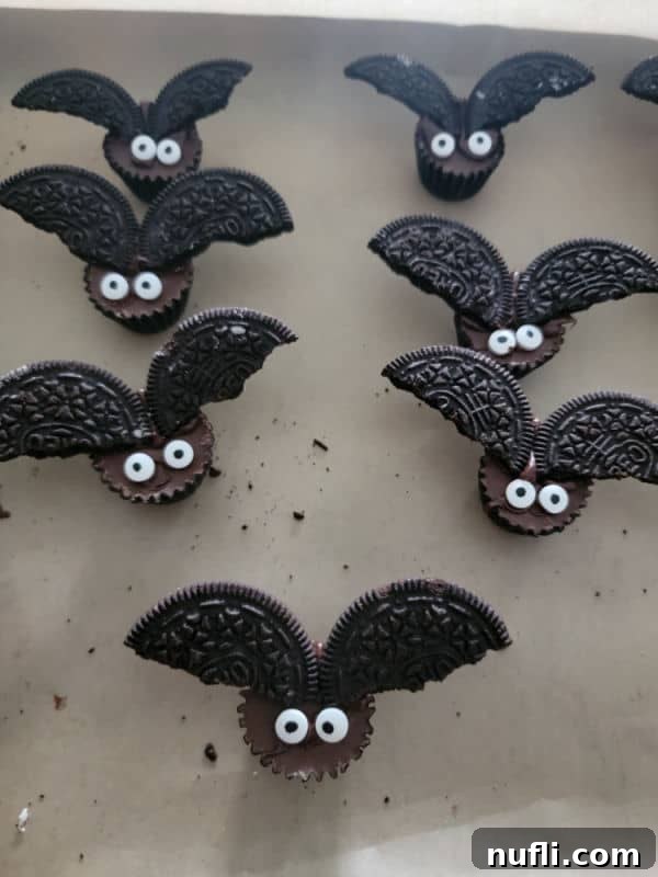 A batch of completed Reese's Bats with candy eyes and Oreo wings, chilling on parchment paper on a baking sheet.