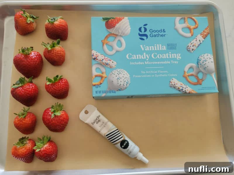 Ingredients for chocolate covered strawberry ghosts: fresh strawberries, white candy coating, and a black icing pen arranged on parchment paper