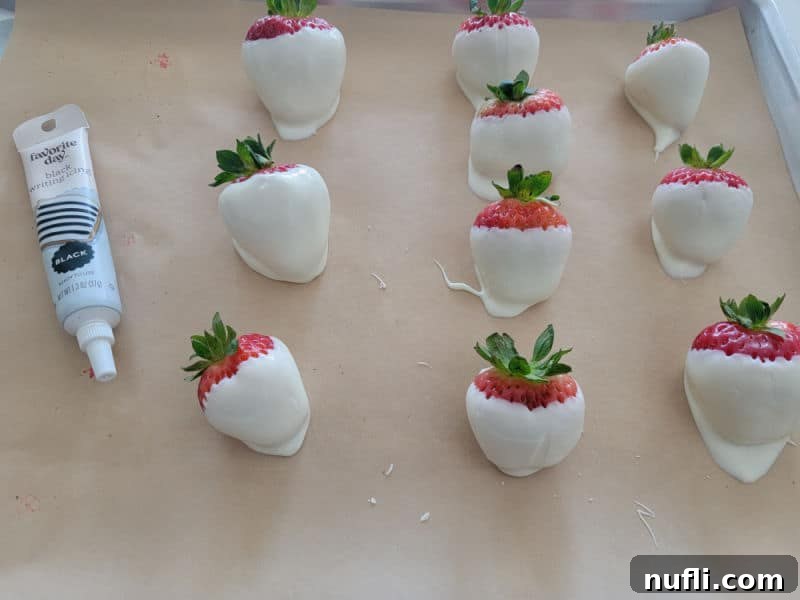White chocolate covered strawberries cooling on a parchment paper lined baking sheet next to a black icing pen