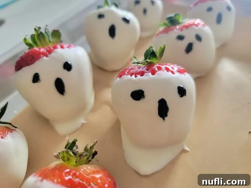 A collection of white chocolate covered ghost strawberries with hand-drawn faces resting on parchment paper