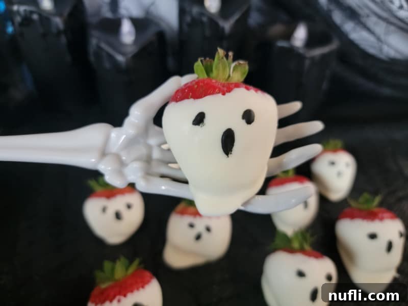 A single white chocolate ghost strawberry held delicately by a skeleton hand, emphasizing its spooky charm