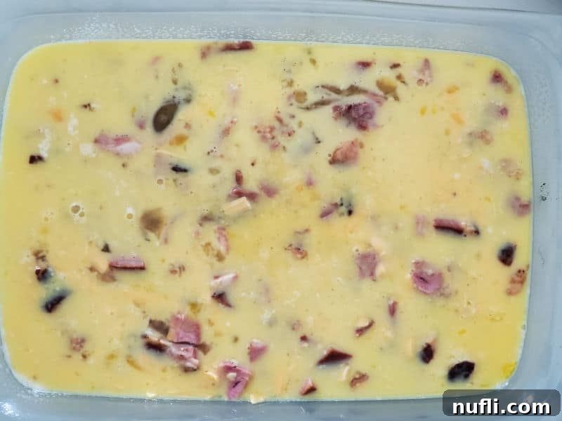 A casserole dish filled with a mixture of whisked eggs, diced ham, and cooked bacon, ready for the tater tot topping.