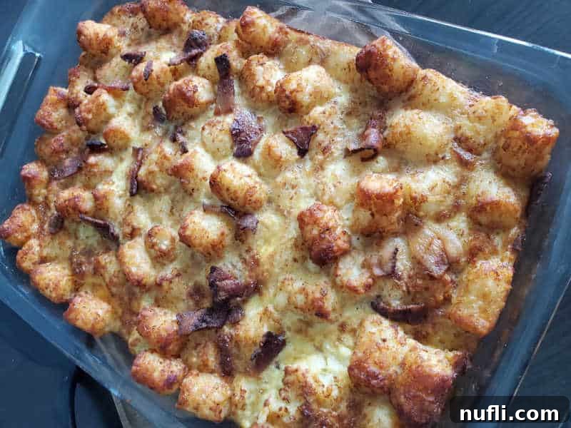 A golden-brown baked Tater Tot Breakfast Casserole with visible crispy bacon and tater tots, fresh out of the oven in a glass casserole dish.