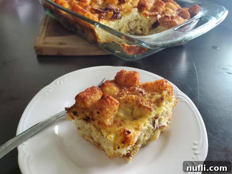 A square portion of Tater Tot Breakfast Casserole on a white plate, positioned next to a glass casserole dish filled with the remaining casserole.