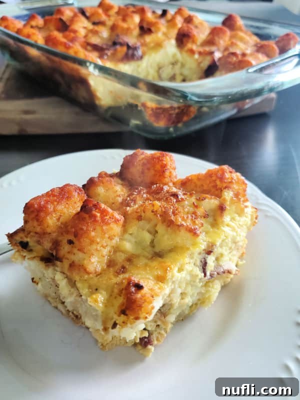 A perfectly baked piece of Tater Tot Breakfast Casserole on a white plate, with the rest of the casserole in a dish on a patterned surface.