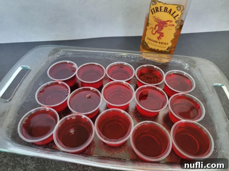 Fireball red jello shots in plastic cups in a casserole dish with a bottle of FIreball