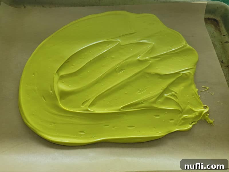 Festive Grinch Bark Made Easy 5 Melted Wilton Vibrant Green Candy melts spread in a oval on parchment paper