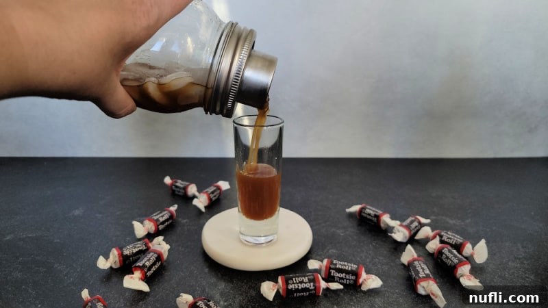 Pouring a Tootsie Roll Shot from a cocktail shaker into a shot glass surrounded by Tootsie Rolls