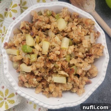 apple stuffing in a white bowl next to a cloth napkin and wooden spoon