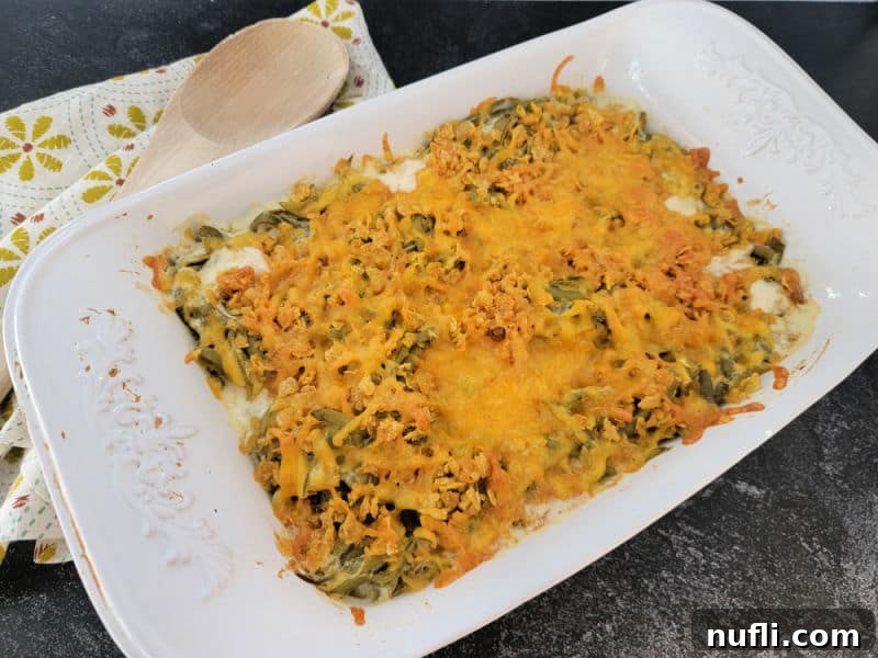Freshly baked cheesy green bean casserole in a white dish, garnished with a wooden spoon and cloth napkin.