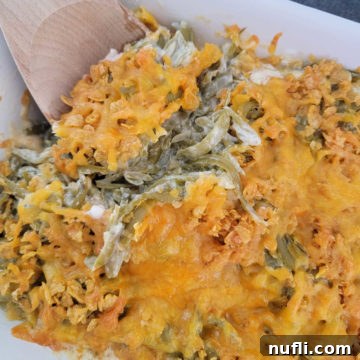 wooden spoon scooping cheesy green beans from a white casserole dish